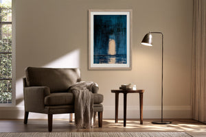 Framed blue abstract artwork with a pale arch above an armchair and side table.