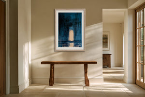 Framed blue abstract artwork with a pale arch hangs above a rustic wooden bench.