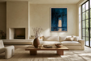Framed blue abstract artwork with a pale arch hangs above a cream sofa near a fireplace.