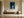 Framed blue abstract artwork with a pale arch displayed above a wooden bench and round vessel.