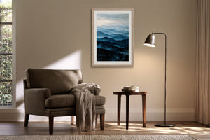 Light wood-framed mountain artwork above an armchair, side table, and black floor lamp.