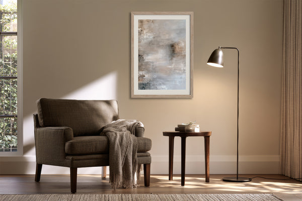 Framed gray-beige abstract artwork above an armchair beside a floor lamp and side table.