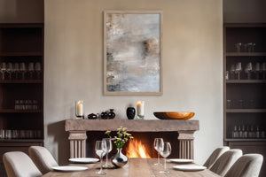 Framed gray-beige abstract artwork above a fireplace and set dining table.