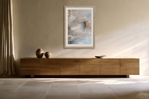 Framed gray-beige abstract artwork above a long wooden sideboard with ceramic vessels.