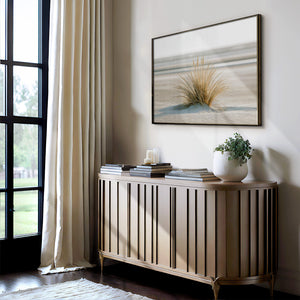 Framed dune grass artwork above a slatted console with stacked books, candles, and a potted plant.