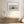 Dune grass artwork in a pale wood frame above a bench with white vases and flowers.
