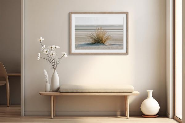 Dune grass artwork in a pale wood frame above a bench with white vases and flowers.