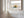 Close view of dune grass artwork in a warm wood frame on a sunlit white paneled wall.