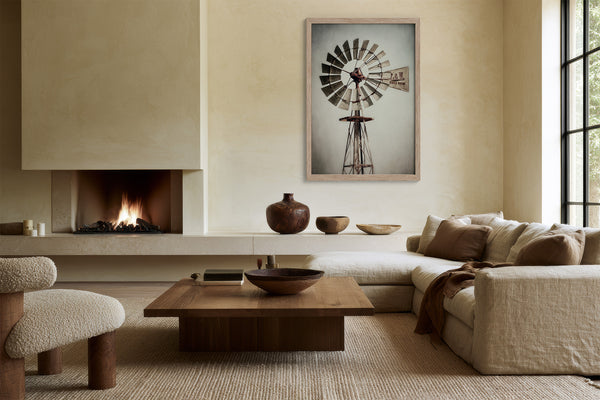 Framed windmill wall art displayed above a low ledge in a living area with fireplace.