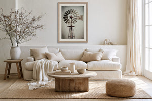 Light wood-framed windmill artwork above a white sofa with a rustic round coffee table.