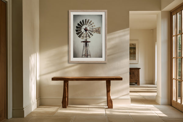 White-framed windmill wall art above a rustic wood console in a sunlit hallway.
