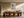 Framed windmill artwork centered above a long wood dining table and sculptural chairs.