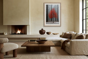 Light wood-framed red-leaved tree artwork above a low sofa beside a lit fireplace.