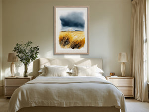 Light wood-framed coastal watercolour of golden grasses and dark clouds displayed above a bed.