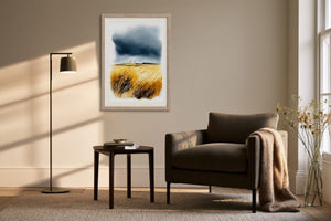 Light wood-framed coastal watercolour above a dark armchair, side table, and black floor lamp.