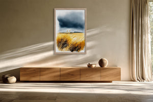 Framed watercolour of golden dune grasses and dark storm clouds above a low wooden sideboard.