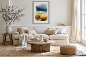 Light wood-framed dune grass watercolour above a cream sofa, with a wood coffee table and woven pouf.