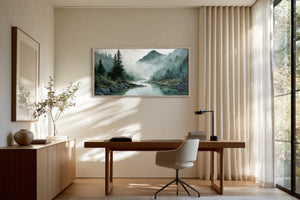 Framed mountain river watercolor above a wooden desk beside tall curtains and large windows.