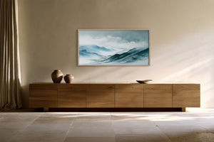 Framed blue and teal watercolor mountain ridges above a long wooden sideboard.
