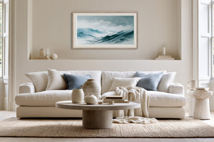 Framed blue mountain watercolor above a cream sofa with pale blue cushions.