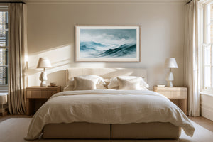 Framed blue mountain watercolor centered above a bed with cream bedding.