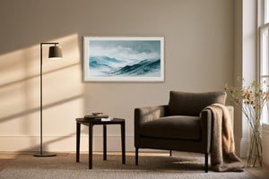 Framed watercolor mountain artwork above a dark armchair, side table, and floor lamp.
