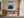 Light wood-framed artwork of a white rowboat on dark water above a wooden desk.