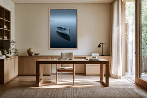Light wood-framed artwork of a white rowboat on dark water above a wooden desk.