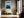 Light wood-framed rowboat artwork above a bench with cushions beside tall windows.