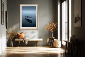 Light wood-framed rowboat artwork above a bench with cushions beside tall windows.