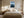 Light wood-framed rowboat artwork centered above a bed with cream bedding and bedside lamps.