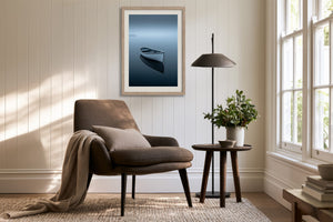 Light wood-framed rowboat artwork above a brown armchair, side table, and black floor lamp.
