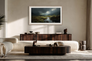 Framed moorland stream artwork above a dark wood sideboard in a sunlit living area.