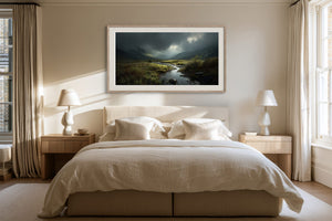 Framed moorland stream artwork centered above a cream bed between matching bedside lamps.