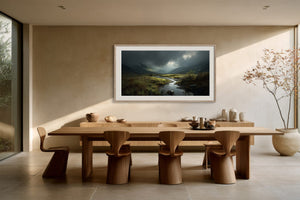 Framed mountain valley stream artwork above a long wooden dining table and sculptural chairs.