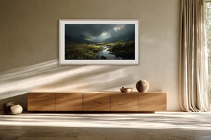 Framed moorland stream artwork above a low wooden cabinet, lit by angled window shadows.