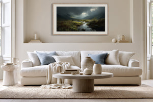 Framed moorland stream artwork above a white sofa with pale blue cushions.