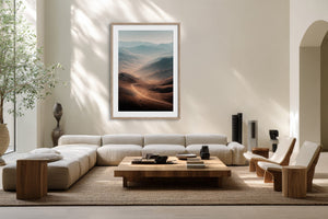 Light wood-framed mountain valley artwork above a low white sofa and wood coffee table.