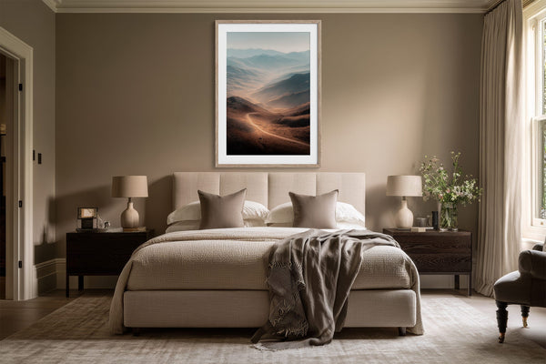 Light wood-framed mountain valley artwork centered above a bed with matching bedside tables.