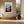 Light wood-framed mountain valley artwork above a built-in bench beside a large ceramic vessel.
