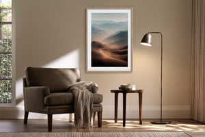 Light wood-framed mountain valley artwork above an armchair, side table, and floor lamp.