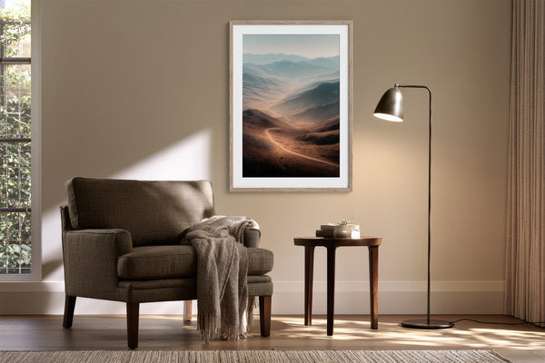 Light wood-framed mountain valley artwork above an armchair, side table, and floor lamp.