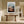Light wood-framed mountain valley artwork above a rustic console table in a sunlit hallway.