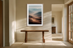 Light wood-framed mountain valley artwork above a rustic console table in a sunlit hallway.