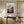 Light wood-framed mountain valley artwork above a wooden desk and upholstered office chair.