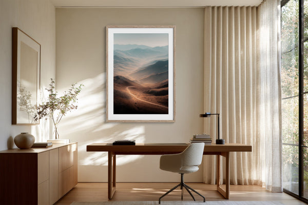 Light wood-framed mountain valley artwork above a wooden desk and upholstered office chair.