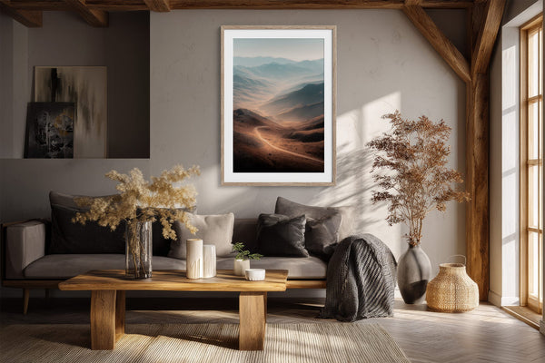 Light wood-framed mountain valley artwork above a gray sofa beneath exposed wooden beams.