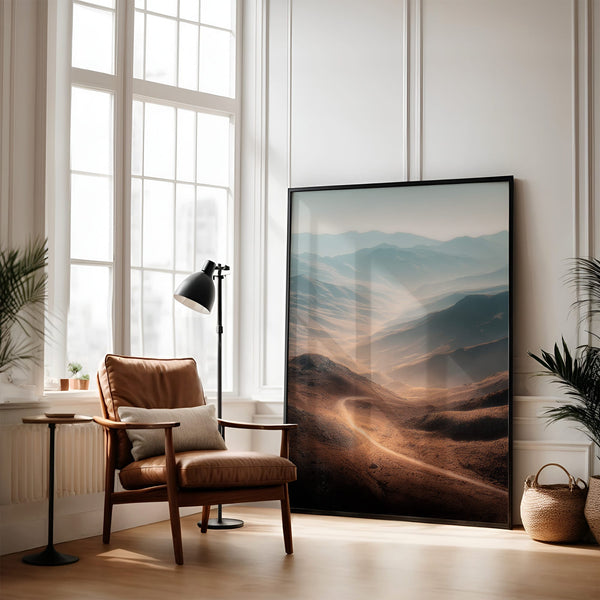 Large black-framed mountain valley artwork leaning beside a leather armchair and floor lamp.