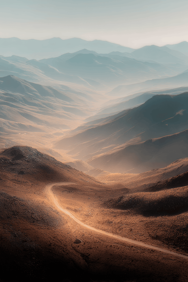 Winding track through a sunlit mountain pass beneath layered blue-grey peaks